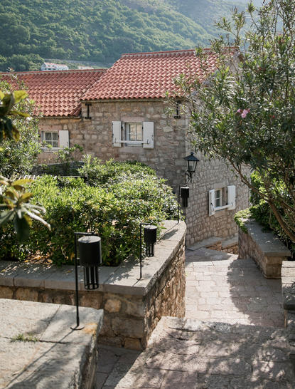 Stone villa with terracotta roof nestled among olive trees at Aman Sveti Stefan, Adriatic coast.