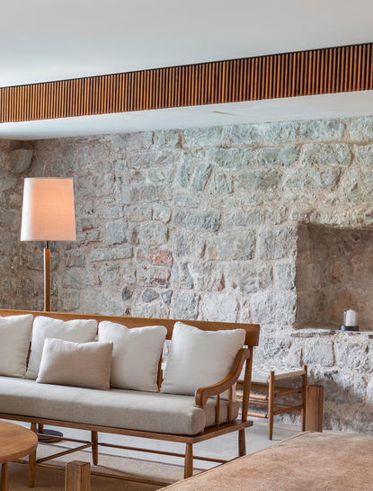 Sitting area at Aman Sveti Stefan with mid-century sofa against stone wall and wooden ceiling detail.