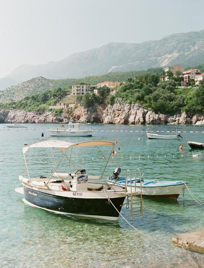 Fishing boats moored in clear turquoise waters at Aman Sveti Stefan, with the stone village and coastline rising beyond.