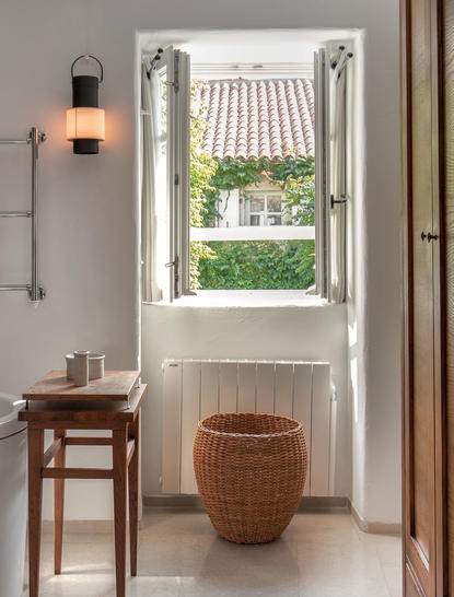 Bedroom nook at Aman Sveti Stefan with shuttered window overlooking village, woven storage basket and wooden side table.
