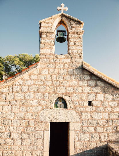 Stone chapel at Aman Sveti Stefan with bell tower and cross, set against clear sky.
