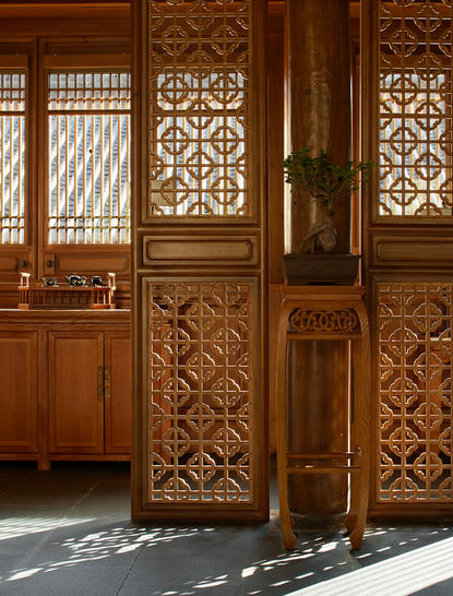 Carved wooden doors with geometric lattice panels at Amandayan, casting geometric shadows on the floor.