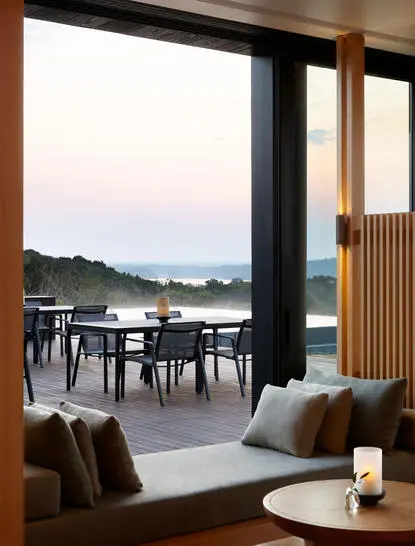 Dining area at Amanemu with open doors revealing coastal views and a terrace seating area.