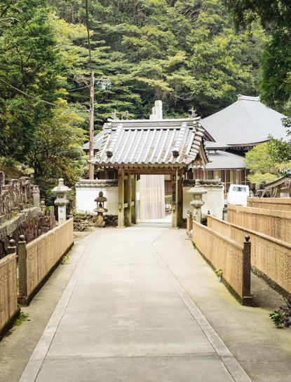 安缦伊沐度假村的传统日式建筑入口，木制栏杆步道通向茅草屋顶的门楼。