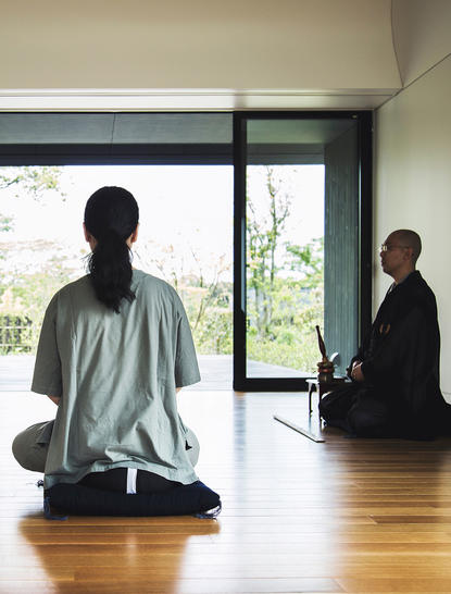 Ospite in meditazione nella sala wellness di Amanemu, con vista sul giardino attraverso le grandi finestre.