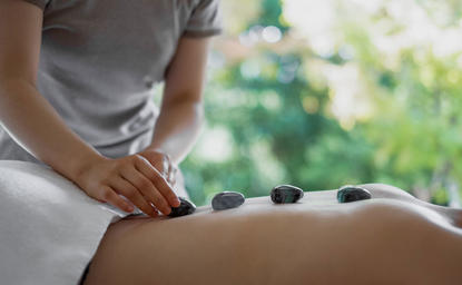 Therapist placing hot stones on a guest's back during a wellness treatment at Amanemu.