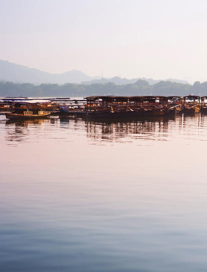 Wooden boats moored on still water at Amanfayun at sunset, mountains visible in the distance.
