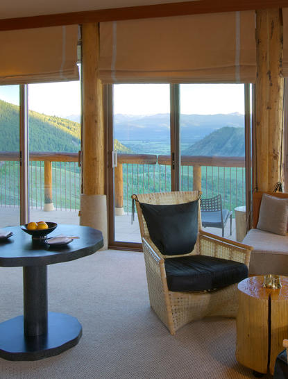 Spring Gulch Suite at Amangani with floor-to-ceiling windows overlooking mountain and lake views, featuring a lounge chair and side table.