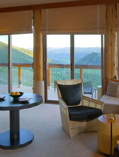 Spring Gulch Suite at Amangani with floor-to-ceiling windows overlooking mountain and lake views, featuring a lounge chair and side table.