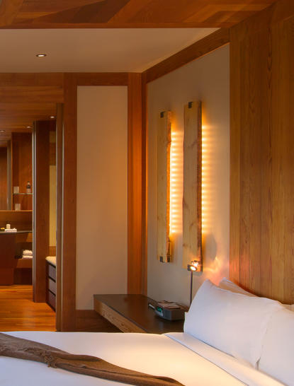Spring Gulch Suite at Amangani with warm wooden interiors and illuminated wall sconces beside the bed.