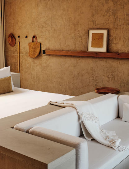 Amangiri Suite with warm terracotta walls, wooden shelf and neutral bedding.
