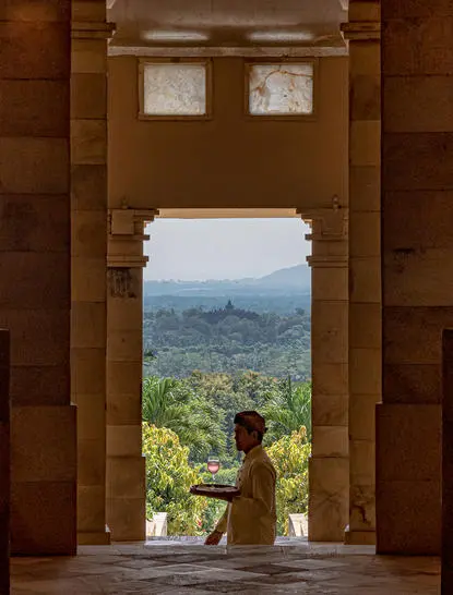 Woman in gold dress seated in stone doorway overlooking Borobudur temple landscape at Amanjiwo.
