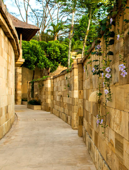 Chemin dallé bordé de murs en pierre et de végétation luxuriante à Amanjiwo resort.