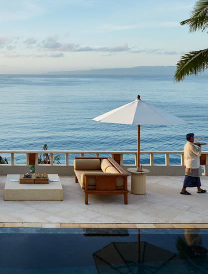 安缦丘澜度假村的套房露台，配有木制家具、遮阳伞和无边泳池，俯瞰宁静的海景。
