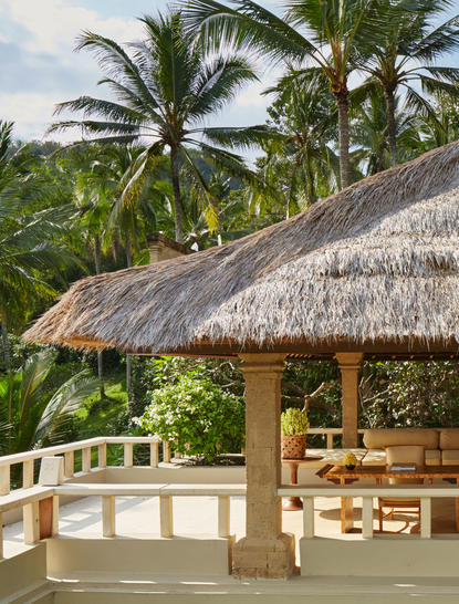 Amankila Resort Garden Suite with thatched-roof pavilion overlooking tropical gardens and palm trees.