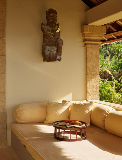 アマンキラ・リゾートのオーシャンスイートの寝室。窓からの自然光が木製ベッドを照らし、壁には彫刻装飾がある。