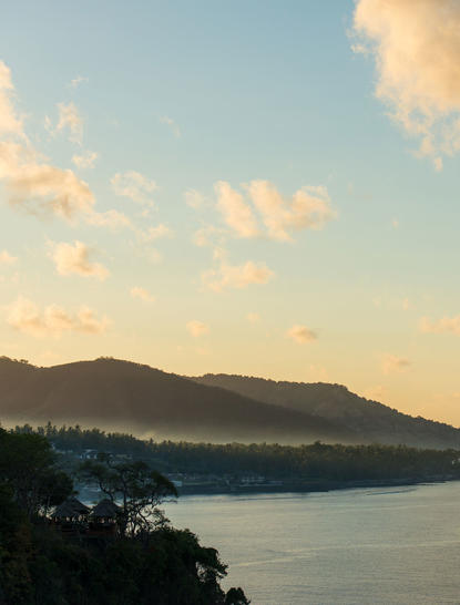 Amankila リゾートの海洋スイートからの眺め。静かな海と遠くの山々が夕焼けに染まっている。
