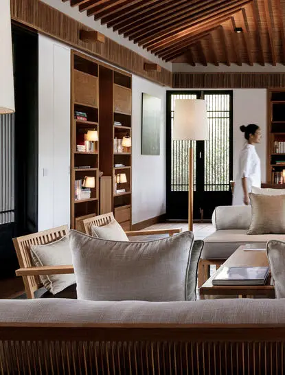 Three-bedroom residence interior at Amanoi resort with cream seating, wooden ceiling, and illuminated display shelving.