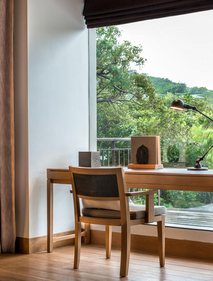 Wooden desk and chair positioned by a large window overlooking Amanoi's verdant landscape.