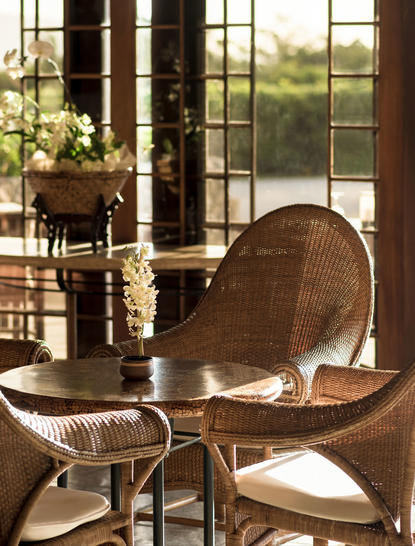 Salle à manger du club-house à Amanpulo, avec fauteuils en rotin et vue sur la nature.
