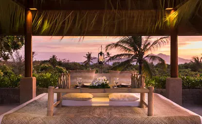 Amanpulo dining clubhouse at sunset, with covered terrace overlooking the water and garden plants.