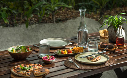 Amanpulo resort의 피크닉 그로브에서 나무 테이블 위에 차려진 야외 식사, 신선한 요리와 물이 담긴 유리병이 놓여 있음.