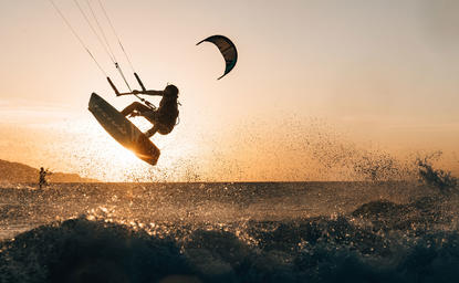 Surfer riding a wave at Amanpulo at sunset with kite visible in golden light.