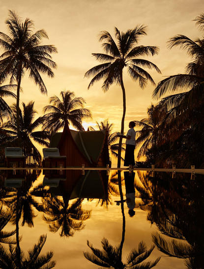 Eight-bedroom ocean villa at Amanpuri with palm trees reflected in still water at golden hour.