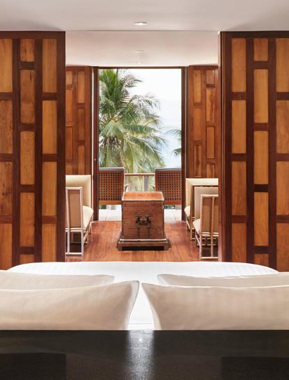 アマンプリのリゾートにある9ベッドルームのオーシャンヴィラの主寝室。木製の装飾的なスクリーンと観葉植物が特徴。