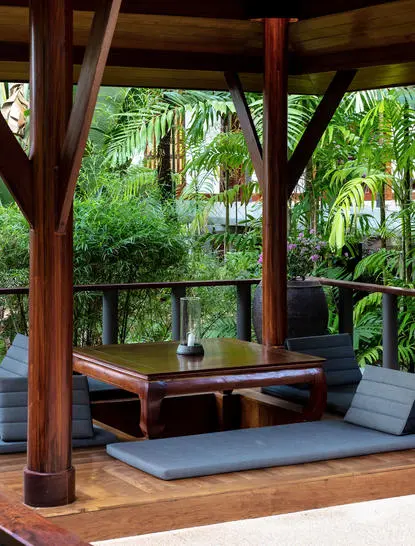 Wooden garden pavilion at Amanpuri resort with open sides, cushioned seating and views into lush tropical greenery.