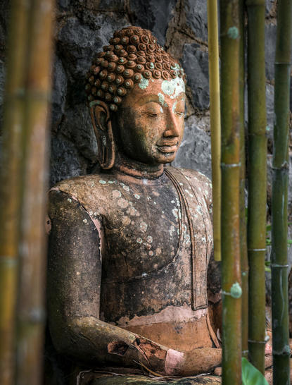 Stone Buddha statue at Amanpuri, partially framed by green wooden shutters.