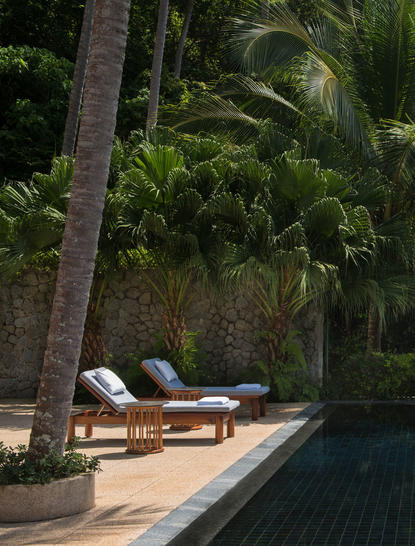 Pool pavilion with wooden loungers and palm trees at Amanpuri.