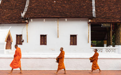 Buddhist monks in saffron robes walking past a whitewashed temple building at Amantaka, Laos.