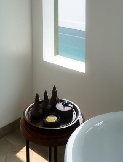 Pool Suite bathroom detail at Amantaka, with round dark wood table and window overlooking water.
