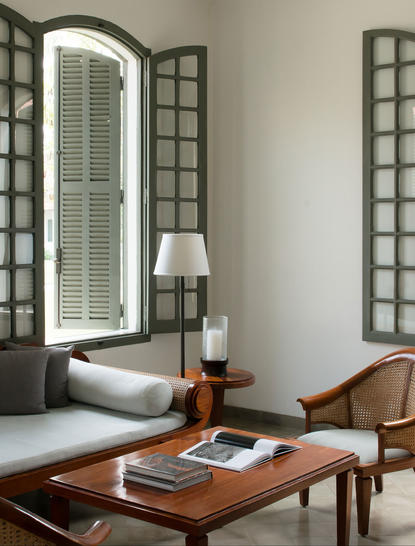 Amantaka suite with wooden desk, chair, and freestanding bathtub beneath tall mirror and windows.
