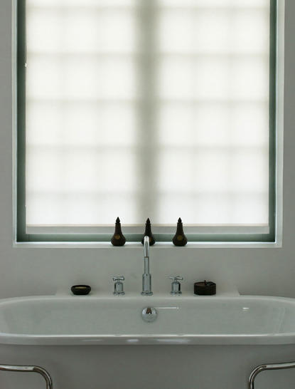 Bathroom vanity with dual taps and mirror at Amantaka, framed by a bright window.