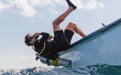 Diver in wetsuit launching backwards off a boat into clear blue water at Amanwana, Indonesia.