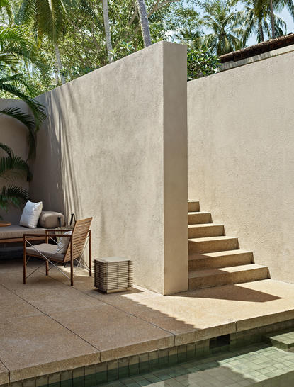 Concrete pavilion with wooden steps at Amanwella, featuring a midcentury chair and potted plants on the terrace.
