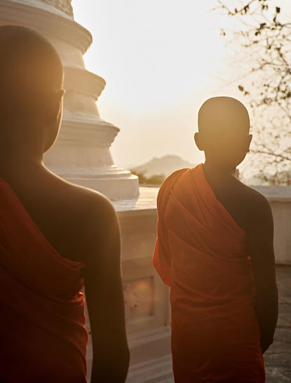 Two monks in saffron robes at Amanwella, silhouetted against golden sunrise light.