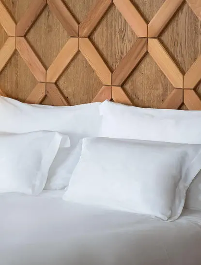 Principal bedroom with geometric wood headboard and white pillows at Aman Le Mélézin.