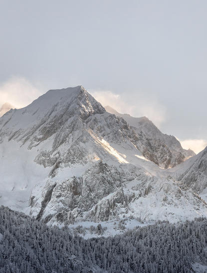 Snow-covered alpine peak above forested slopes at Aman Le Mélézin, France.