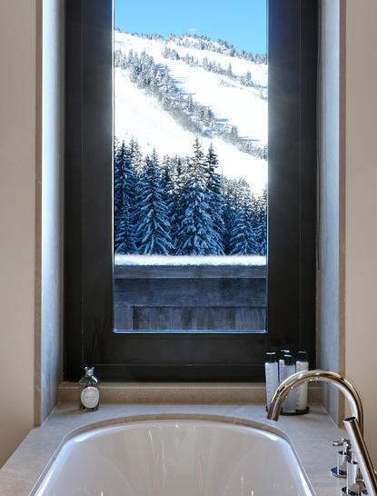 Freestanding bathtub positioned before a window framing snow-covered Alpine slopes at Aman Le Mélézin, France.