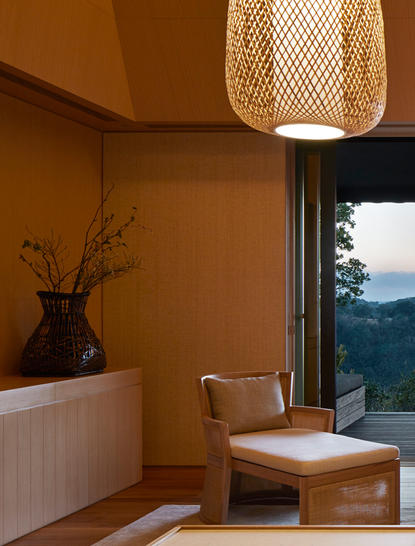Living area at Amanemu with woven pendant light, wooden chair, and views towards mountains.
