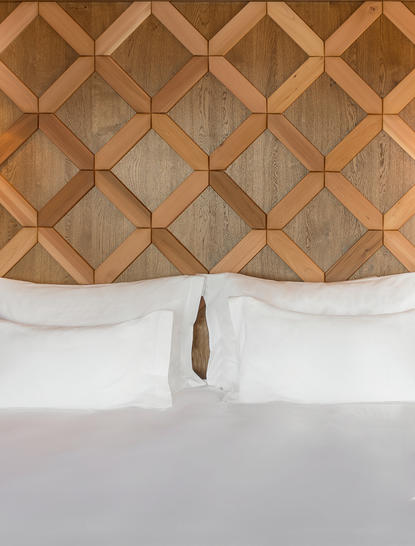Principal bedroom headboard detail at Aman Le Mélézin, featuring geometric wooden panelling above white bedding.