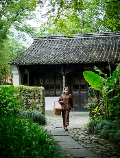 Woman walking through traditional Chinese pavilion surrounded by lush greenery at Amanfayun.
