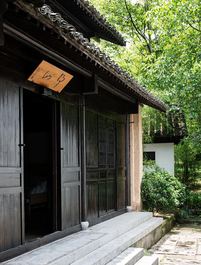 Timber pavilion entrance with dark wooden doors and grey stone platform at Amanfayun.