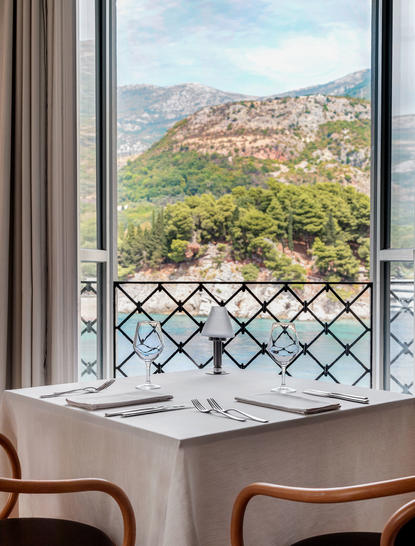 Dining area at Aman Sveti Stefan with views of the Adriatic coastline and hillside beyond latticed doors.