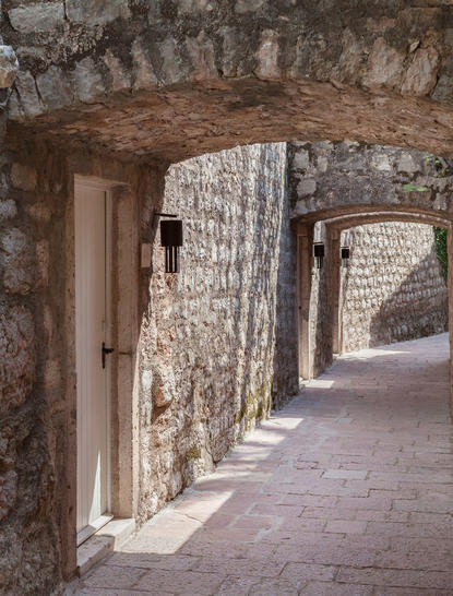 Stone corridor with weathered arches at Aman Sveti Stefan, morning light casting shadows on aged walls.