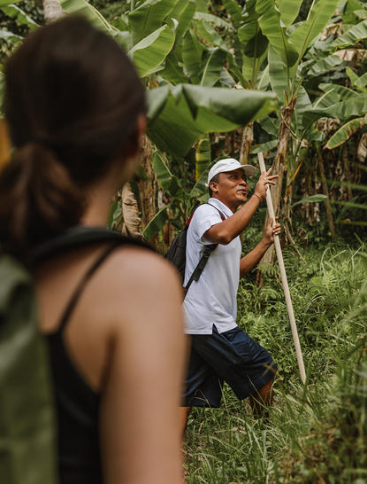 Cyclist riding through lush green vegetation at Amandari, with companion in foreground.