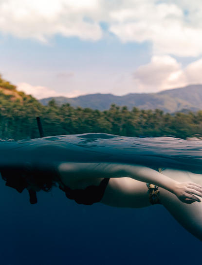 Person paddling outrigger canoe on calm waters at Amankila, with forested mountains beyond.